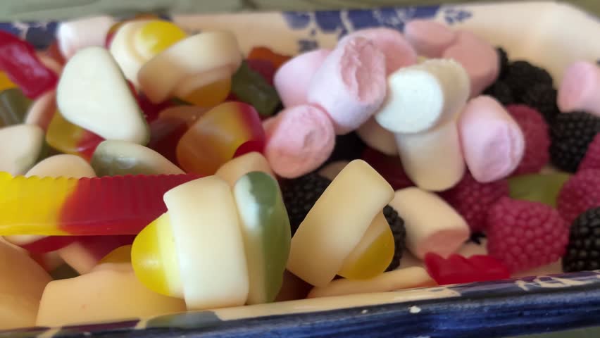 A vibrant macro close-up photograph capturing a diverse assortment of colorful gummy candies and jelly sweets. The image highlights the sugary coating, translucent textures, and bright assorted shapes including gummy bears
