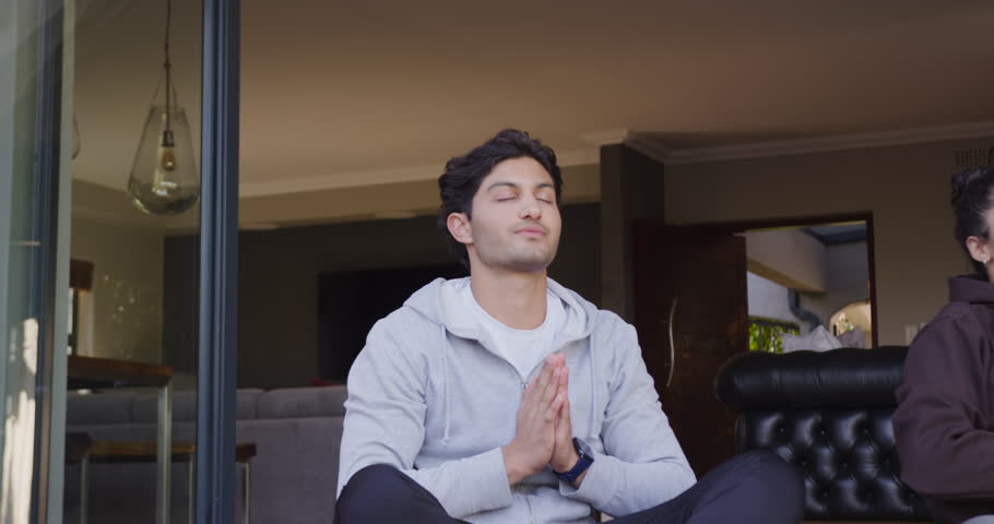 Man entering sliding doorway and sitting cross-legged, pressing palms, meditating near sofa. Threshold, meditation, mindfulness, serene, calm, seated, pose