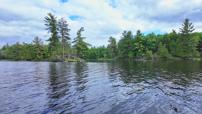 POV view moving boat gliding over rippling blue water. Gentle waves under a cloudy sky as the camera drifts steadily forward. Calm, cinematic lakeside backdrop.