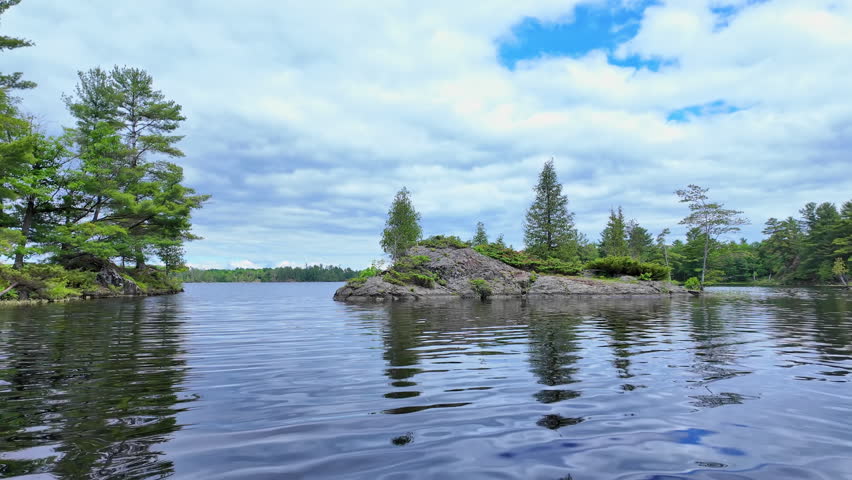 POV view moving boat gliding over rippling blue water. Gentle waves under a cloudy sky as the camera drifts steadily forward. Calm, cinematic lakeside backdrop.