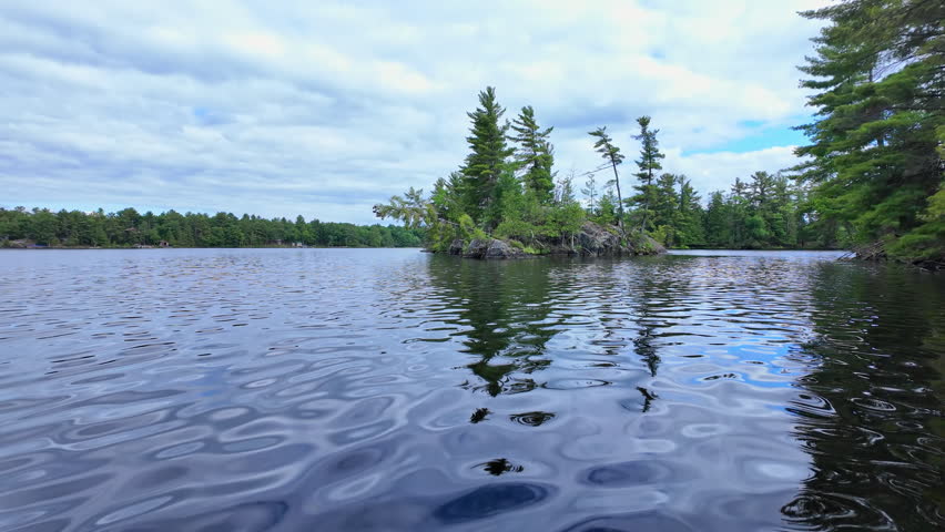 POV view moving boat gliding over rippling blue water. Gentle waves under a cloudy sky as the camera drifts steadily forward. Calm, cinematic lakeside backdrop.