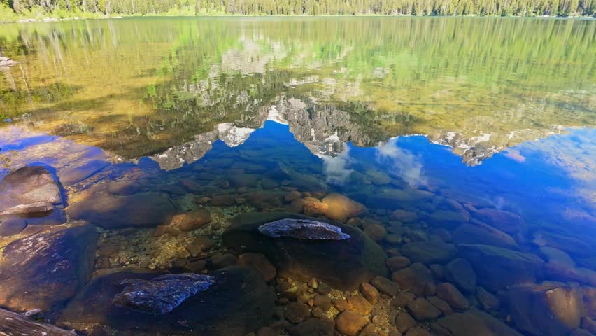 Calm waters of Bradley Lake perfectly mirror the rugged snowcapped Teton peaks above