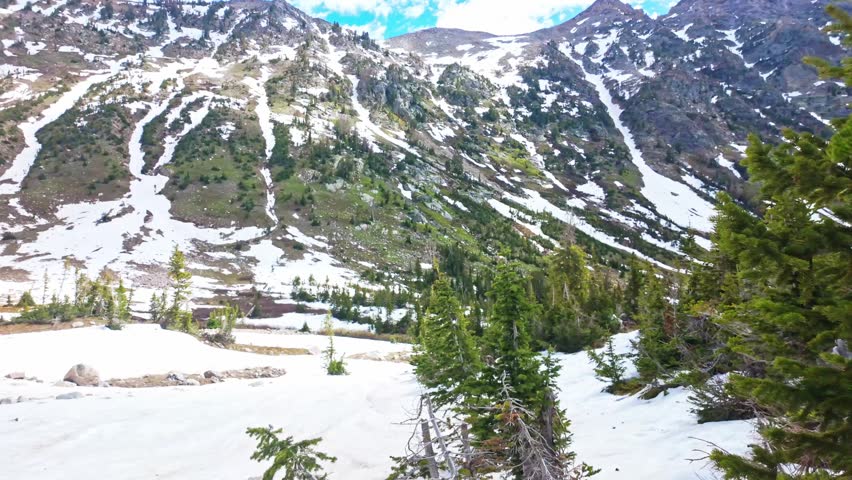 Sweeping panoramic view of the Teton mountain range with a snow covered trail leading to Solitude Lake