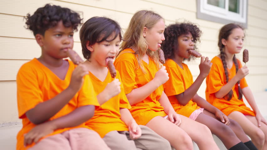 Group of Happy diverse children kids enjoying eating ice cream together outdoors during summer break sharing friendship happiness and carefree childhood while sitting outside after school activities.