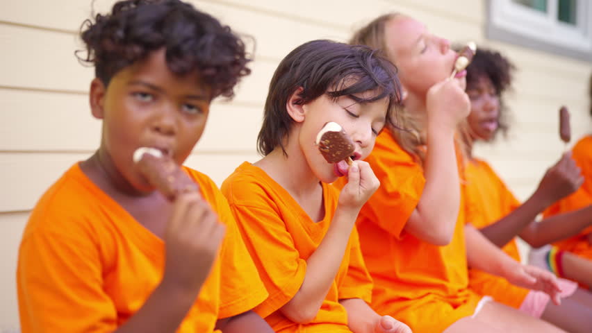 Group of Happy diverse children kids enjoying eating ice cream together outdoors during summer break sharing friendship happiness and carefree childhood while sitting outside after school activities.