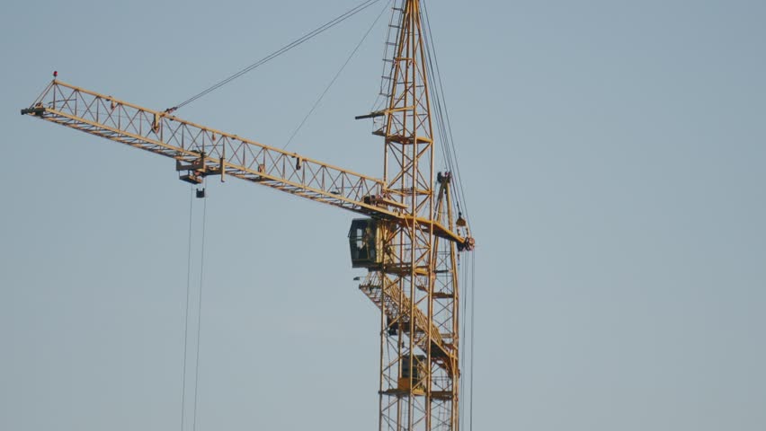 Yellow tower crane positioned next to an unfinished concrete high-rise. Shows the interaction between the metal lattice