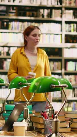 Vertical screen: Woman tutor speaking with students seated around library table with books, showing study support, group research and university classwork.