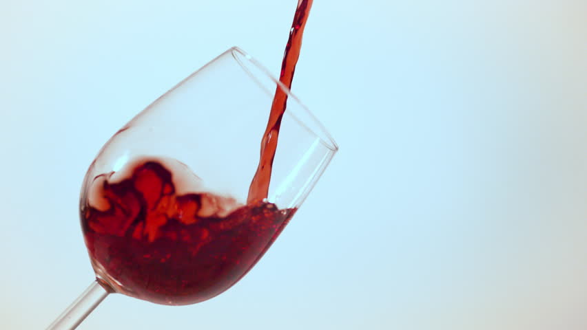 Cluj, Romania - 13.07.2017: Studio ultra slow motion of red wine pouring and splashing in a tilted wine glass on a clean background.