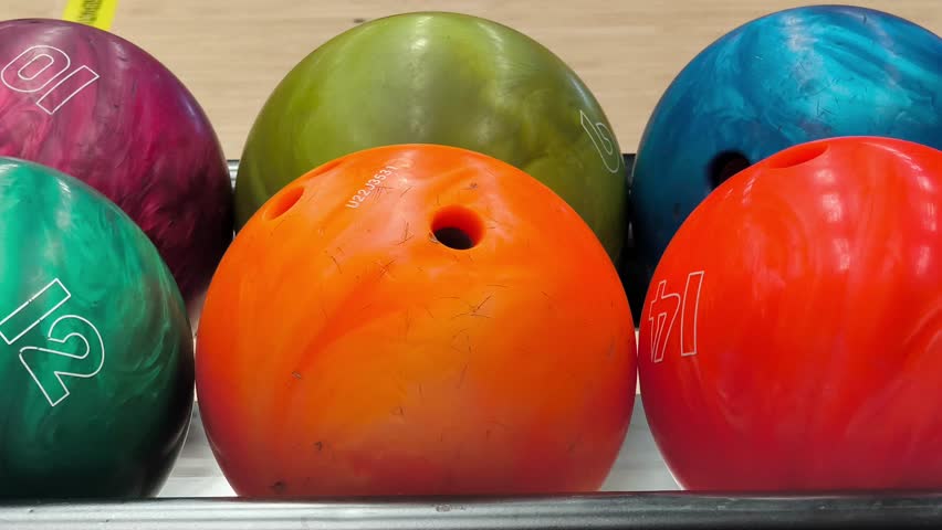 Multi-Colored Bowling Balls Rotating on Automatic Return Rack. A close-up shot of vibrant, multi-colored bowling balls rolling back on an automatic ball return system at a bowling alley. Perfect for sports and recreational concepts. Sports video, 4k, 60 fps.