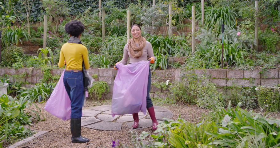 Arriving terraced garden, Diverse women holding purple bags wearing orange gloves collecting waste. Outdoor, volunteers, collaboration, greenery, plants, path, boots