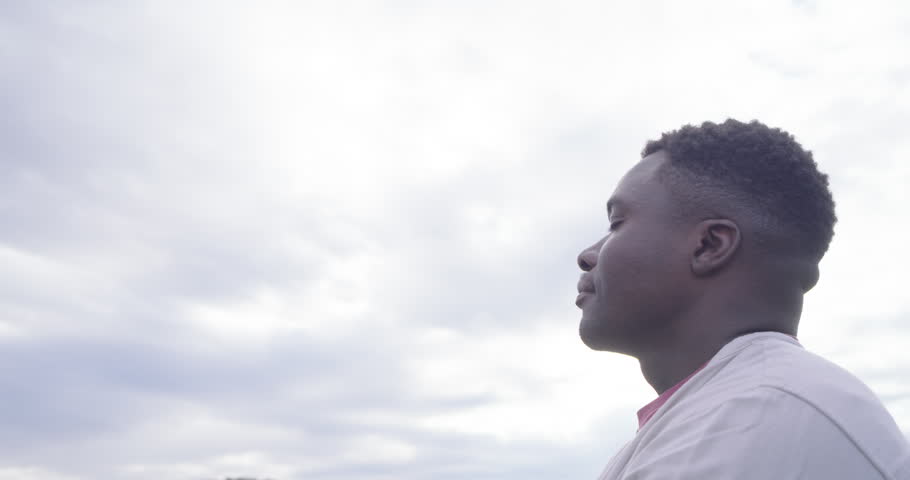 African man turning, facing camera and smiling in light jacket, cloudy sky, treeline, copy space. Portrait, outdoor, overcast, field, nature, calm, confident