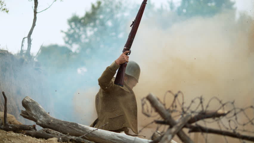 Historical military reenactment featuring a soldier lifting rifle amid smoke, barbed wire in slow motion.