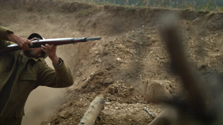 Historical reenactment featuring a soldier who recoils and falls back in a dusty trench under fire