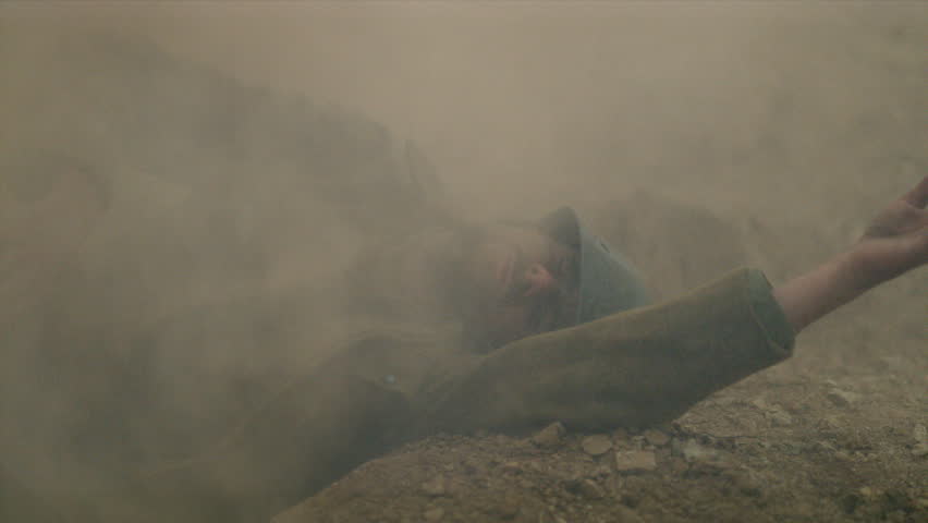 Soldier standing in a trench during a historical battlefield reenactment, crawling along rocky ground through thick smoke and dust.