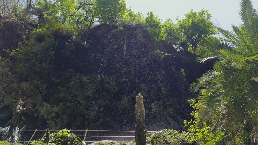 Pan down shot from water droplets falling off plant covered hills to path below near hot sulphur water springs of Sahastradhara Dehradun a popular tourist and religious destination