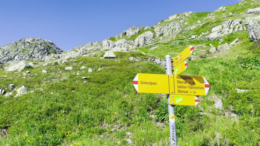 Yellow Swiss hiking signpost pointing to Grimselpass, Oberaar and Sidelhorn on a flowering alpine meadow below granite slopes near Grimsel Pass in the Bernese Alps of Switzerland