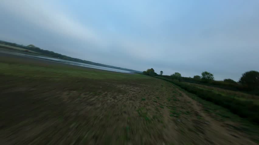 Low angle FPV drone point of view flying fast over a large lake with wild ducks taking off under gloomy autumn skies.
