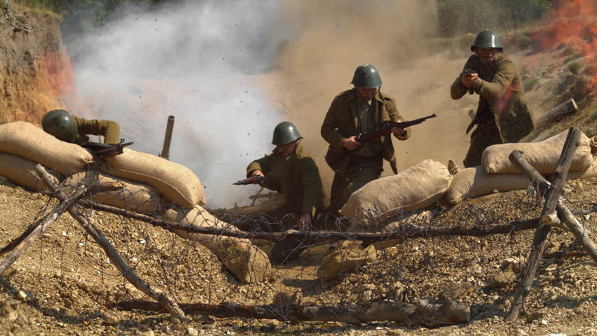 Soldiers advance in a trench with sandbags, barbed wire, smoke and explosions during a historical military reenactment, ultra slow motion.