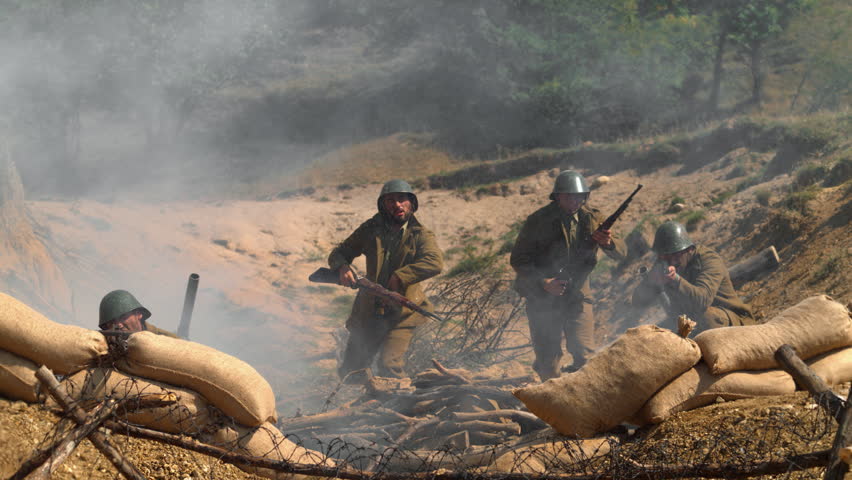 Historical military reenactment showing infantry advance through smoke and dust behind sandbags in a trench line, captured in ultra slow motion.