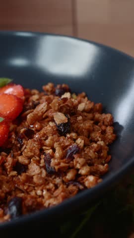 Close-up view of a breakfast bowl with crunchy granola, fresh sliced strawberries, yogurt and mint leaves.