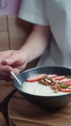 A person scoops a spoonful of creamy rice porridge topped with fresh strawberries, nuts and mint leaves.