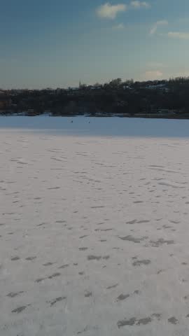 Two people traverse a snowy frozen lake, surrounded by distant hills and a clear sky, showcasing the beauty of winter outdoors