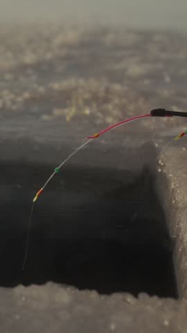 Fishing line with bait is lowered into an ice hole, followed by a fish being pulled out in a snowy winter environment