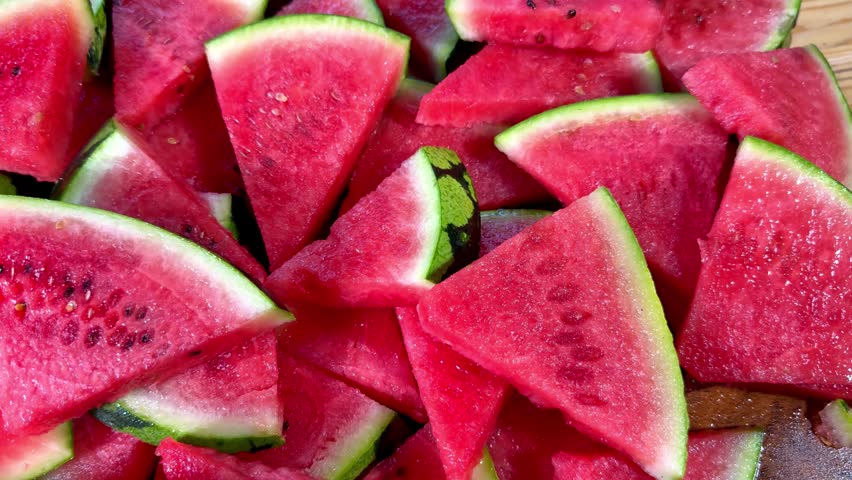 Closeup pan shot of water melon or watermelon, which has been cut into triangular slices, with thick green outer skin and juicy pink fruit, ready to eat.