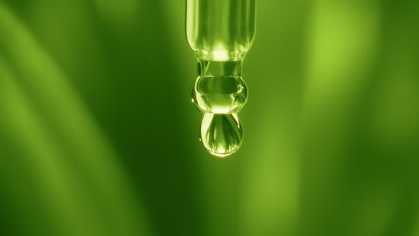 Macro shot of a clear plant extract or tea tree oil droplet falling from a glass pipette with a blurred green leaf background in slow motion