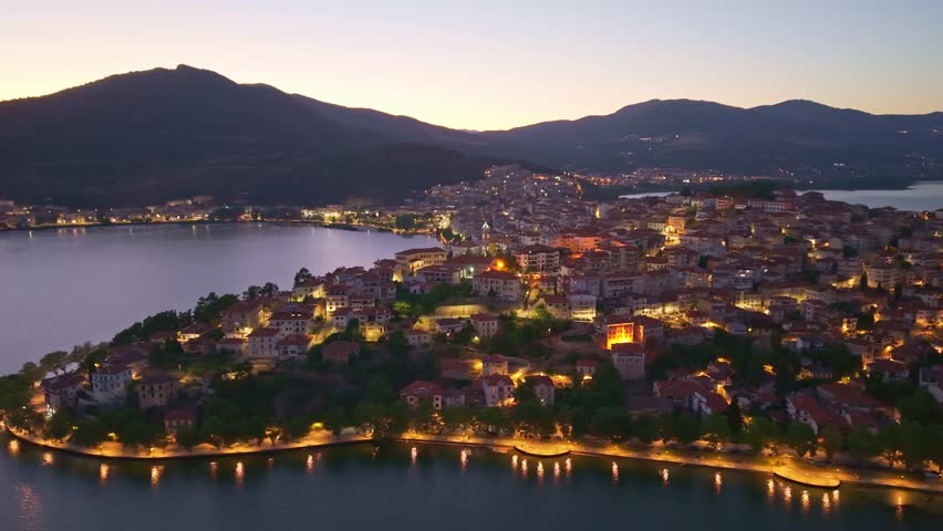 Beautiful night aerial view of Kastoria city lights reflecting in Lake Orestiada with mountains in the background at dusk, Greece
