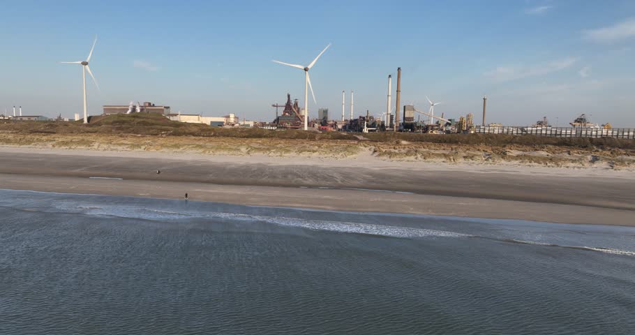 Drone view of a beachside near an industrial zone at Ijmuiden, and rotating windshields and blast furnaces in the background in Netherlands