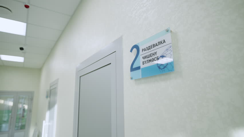 Glass directional sign hangs near door leading to changing room. Navigation within contemporary sports complex for visitors convenience