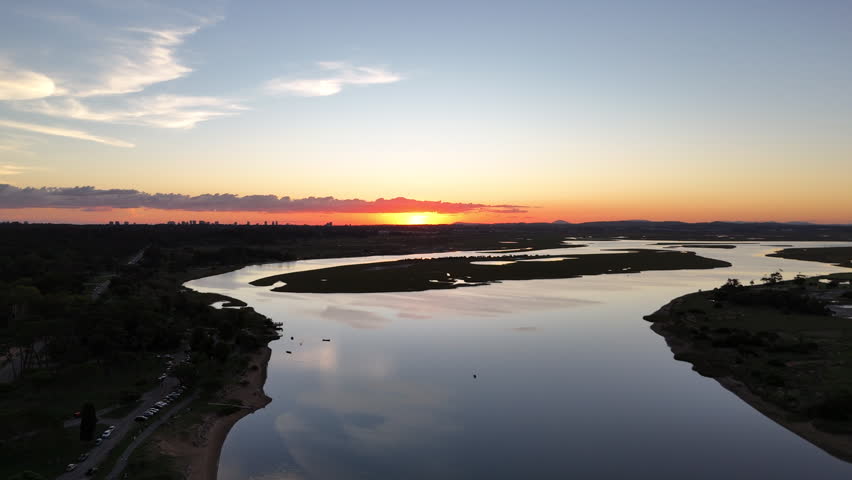 Aerial drone view of a golden sunset over winding wetlands and calm river landscape near Punta del Este, Uruguay, with colorful sky reflections and peaceful natural scenery.