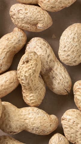 unshelled peanuts rotating on a rustic kitchen tabletop. Natural whole peanuts in shells arranged in a scattered composition, showcasing organic texture and freshness. Premium 4K food video ideal for healthy eating, agriculture, snack, ingredient, harvest, and food industry concepts