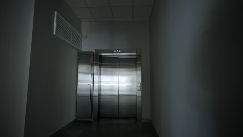 Sleek metal elevator doors stand centered in dimly lit corner hallway. Digital indicator displays floor number. Modern design of interior
