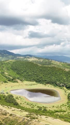 Scenic mountain lake landscape with a dramatic cloudy sky and green rolling hills, featuring a peaceful pond reflecting the clouds in a beautiful and serene natural environment
