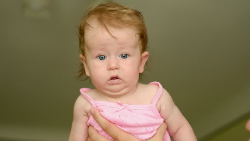 Happy mother holding her cute baby girl in pink bodysuit at home. Loving family lifestyle concept.