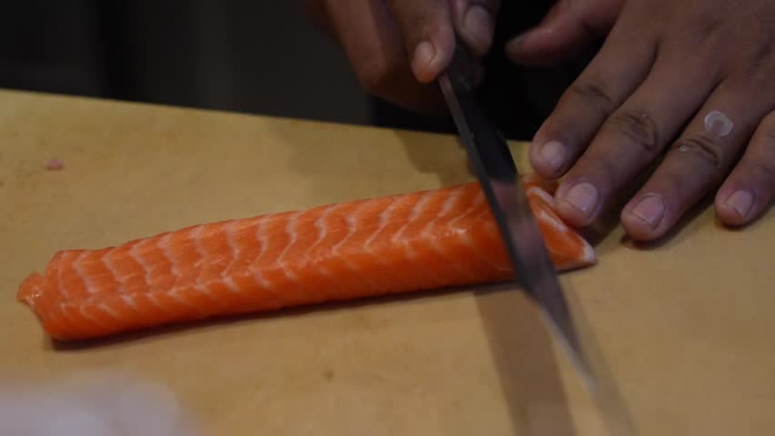 Chef slicing fresh salmon fillet for sushi and sashimi, showcasing precision knife skills in close-up professional kitchen footage.