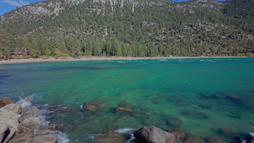 Clear turquoise water of Lake Tahoe with rocks and gentle waves near shoreline in California. Scenic mountain lake landscape with forested hills, ideal for travel, nature, and outdoor use