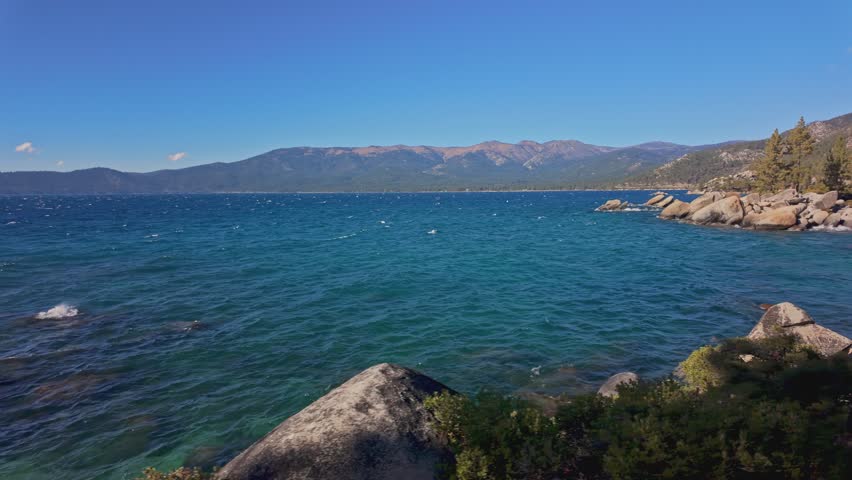 Blue water of Lake Tahoe with rocky shoreline and mountains in California. Scenic natural landscape with clear sky and waves, ideal for travel, nature, and outdoor use