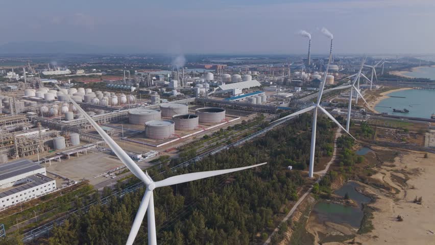 Aerial footage of wind turbines on the coast of Dongfang city, Hainan Island, with petrochemical factory in the background.