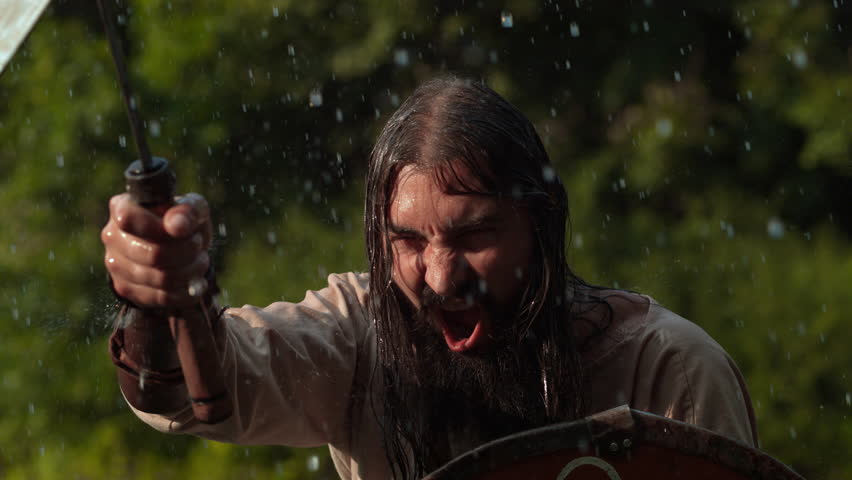 Dacian warrior yells in the rain, raising a sword and shield during a historic battle reenactment.