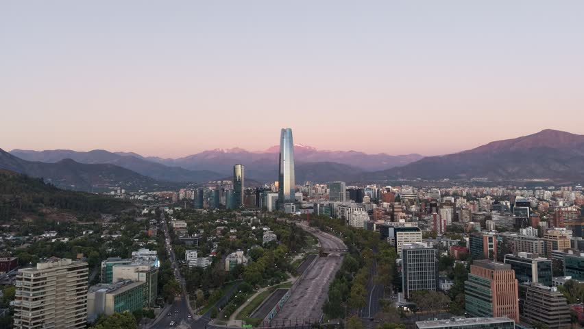 Aerial horizontal tracking shot of Santiago city skyline with the Andes mountains during dusk