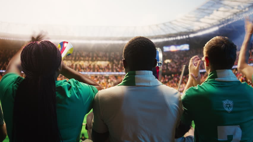 Soccer supporters cheer in packed stadium stands during a football match, creating loud crowd energy and team support.