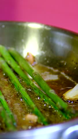 Asparagus frying with garlic and lemon in stainless steel pan as chef turns each spear with spatula in warm kitchen close up healthy side dish