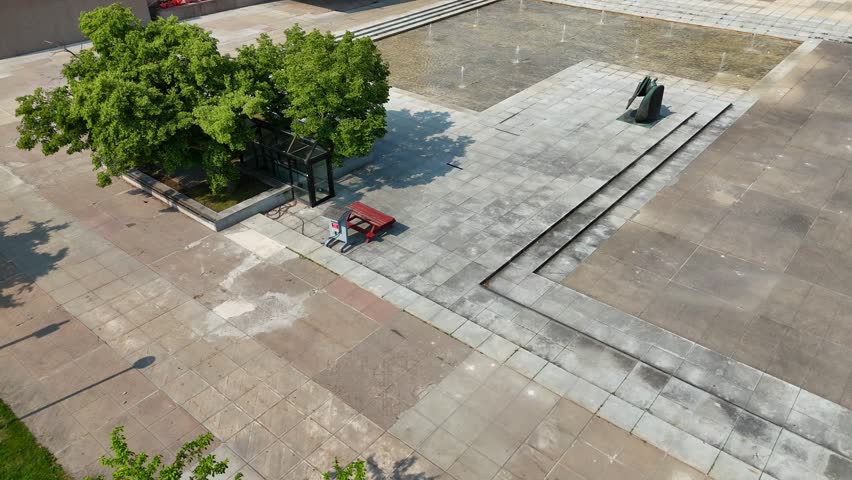 An open plaza and a large, shallow pool with numerous water jets dispensing water into the air sits adjacent to a building dedicated to being a museum on a beautiful sunny summer day.