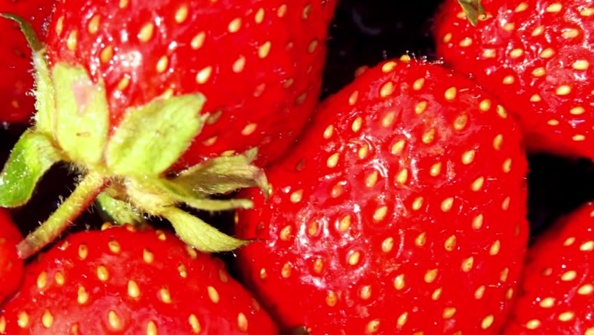 Extreme close-up footage of ripe, juicy red strawberries rotating slowly. The macro lens highlights the vibrant color, seeds, and fresh green leaves of this delicious summer berry. 