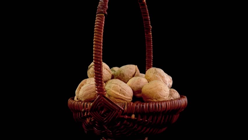 A traditional, rustic scene featuring fresh whole walnuts inside a beautiful woven brown basket, isolated on a black background. Ideal for harvest, farming, and organic food visuals. 