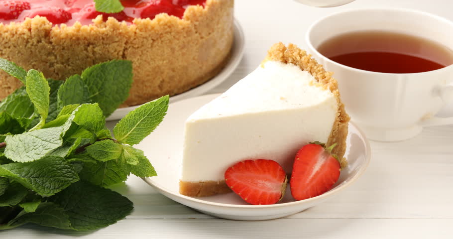 Pouring strawberry jam onto piece of cheesecake at white wooden table, closeup