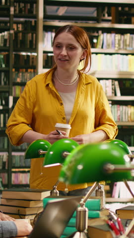 Vertical frame: A tutor in yellow speaks to university students gathered at library table, connecting classmates, open books and focused education work.